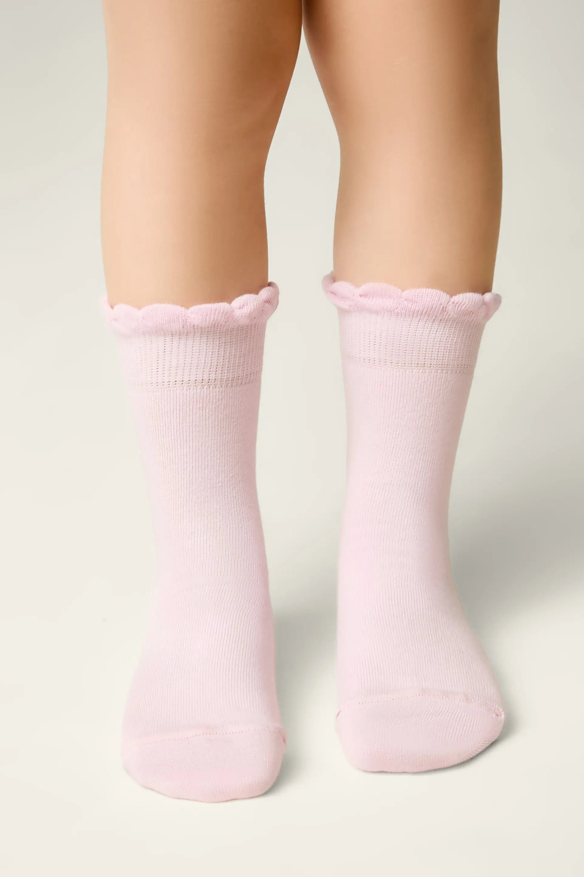 Pink socks with scalloped edges worn by a person on a light gray background #color_light-pink
