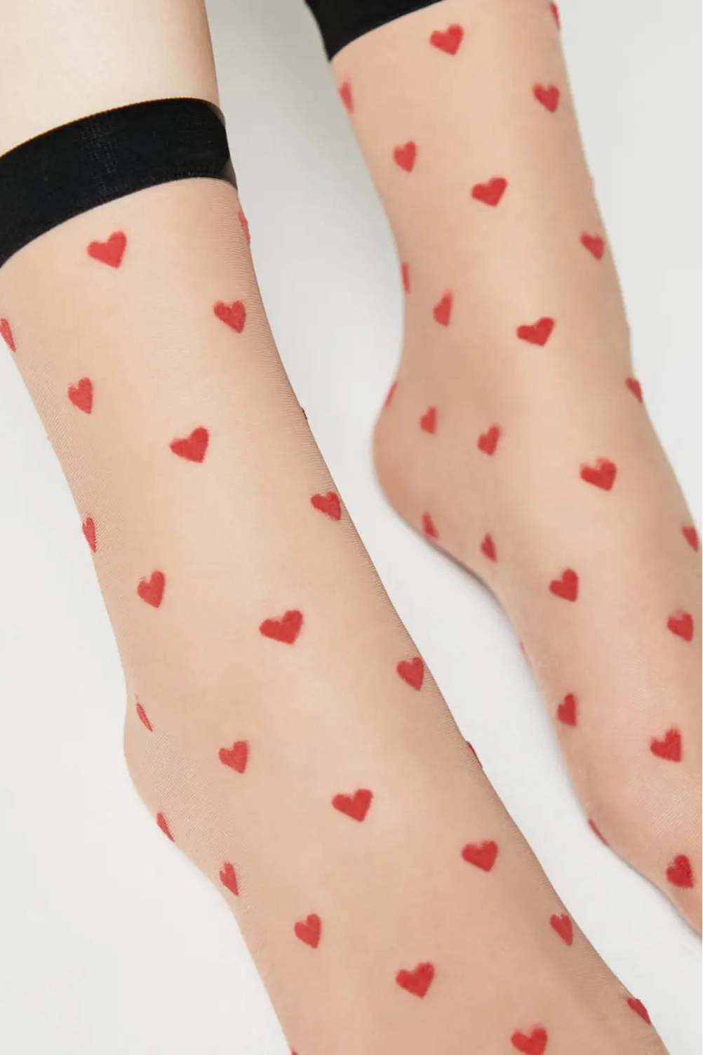Sheer socks with red heart patterns worn by a person on a light background #color_natural-nude