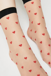 Sheer socks with red heart patterns worn by a person on a light background #color_natural-nude