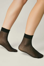 Black fishnet socks worn by a person on a neutral background #color_nero-black