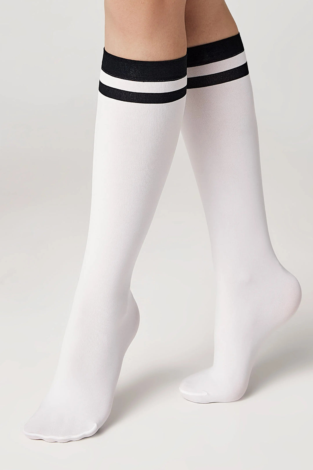 White knee-high socks with black stripes worn by a person on a light gray background