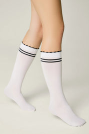 White knee-high socks with black stripes worn by a person on a light gray background