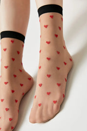 Sheer socks with red heart patterns worn by a person on a light background #color_natural-nude