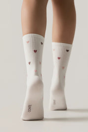 White socks with heart patterns worn by a person on a light gray background #color_milky