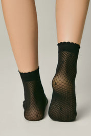 Black fishnet socks worn by a person on a plain background #color_nero-black