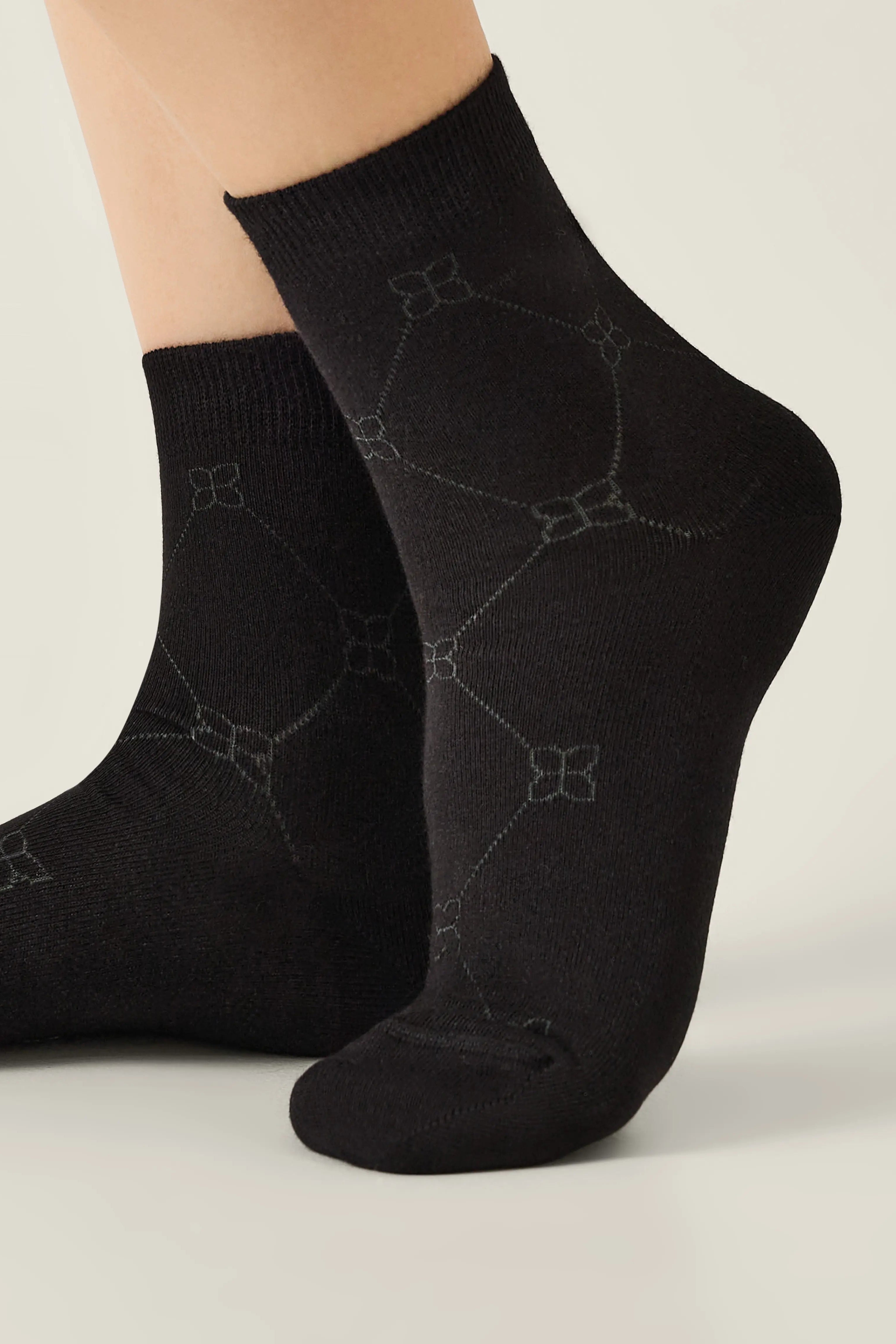 Black socks with subtle pattern worn by a person on a light gray background #color_black