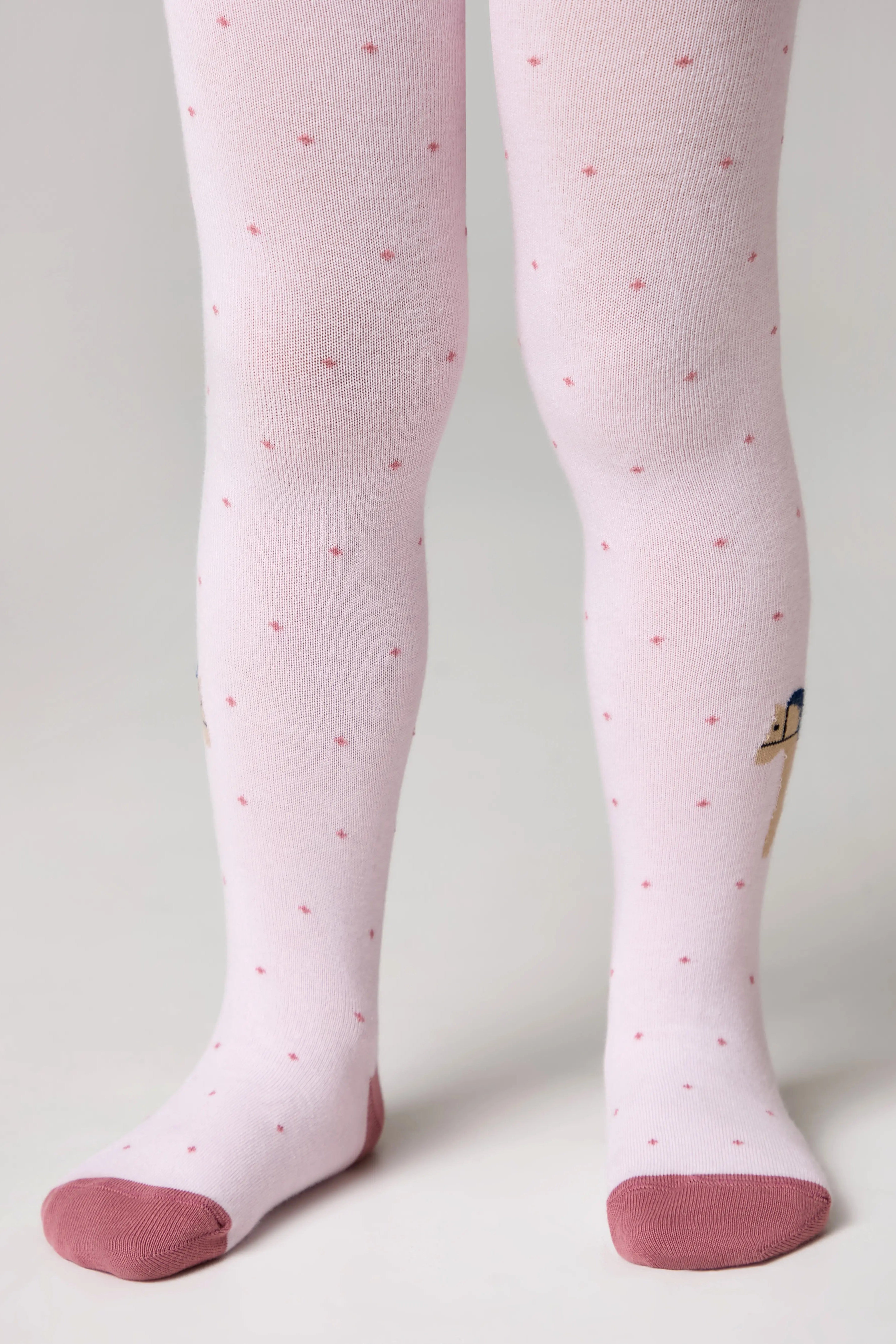 Pink tights with red polka dots worn by a person on a light gray background #color_light-pink