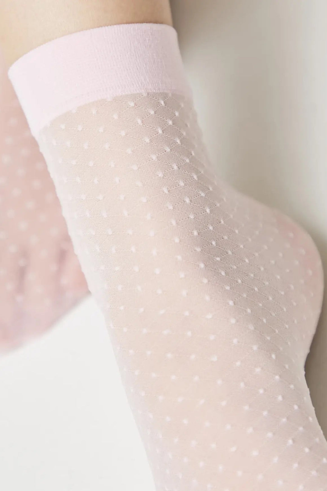 Sheer white stockings with a subtle pattern worn by a person against a neutral background #color_light-pink