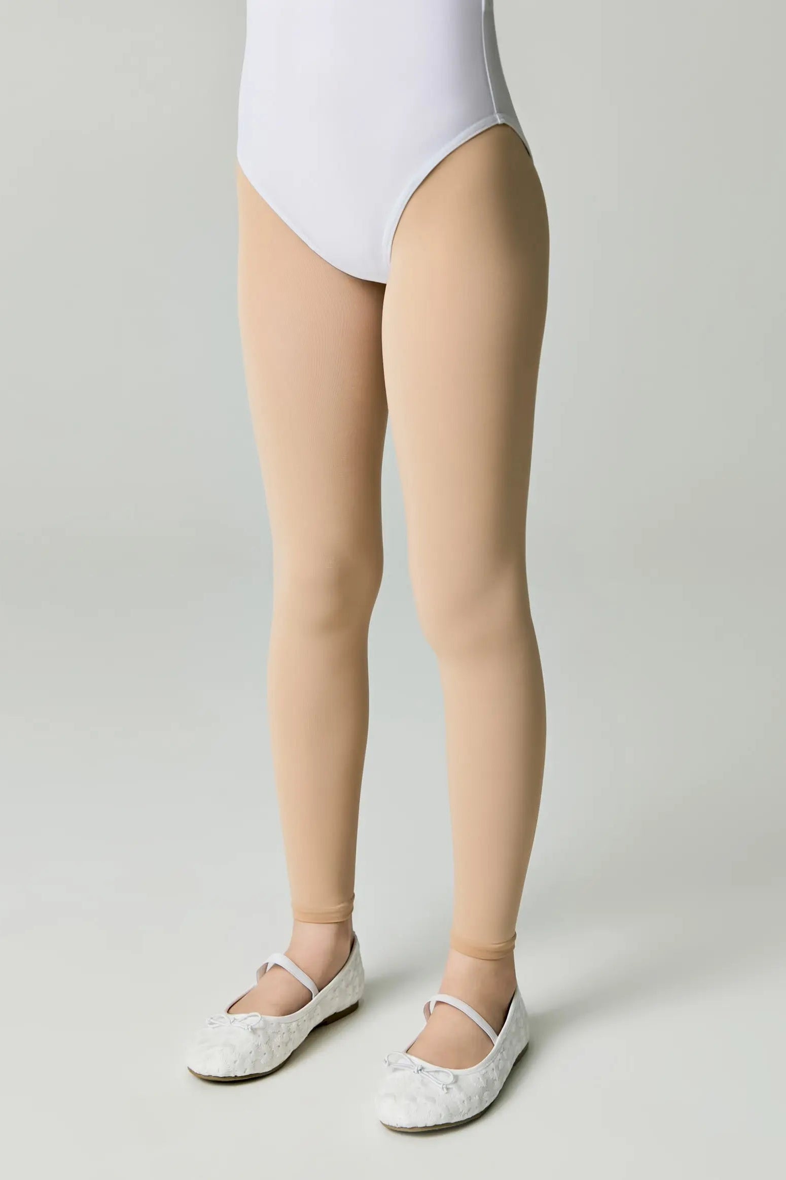 Person wearing a white bodysuit and beige tights on a plain background #color_natural-nude