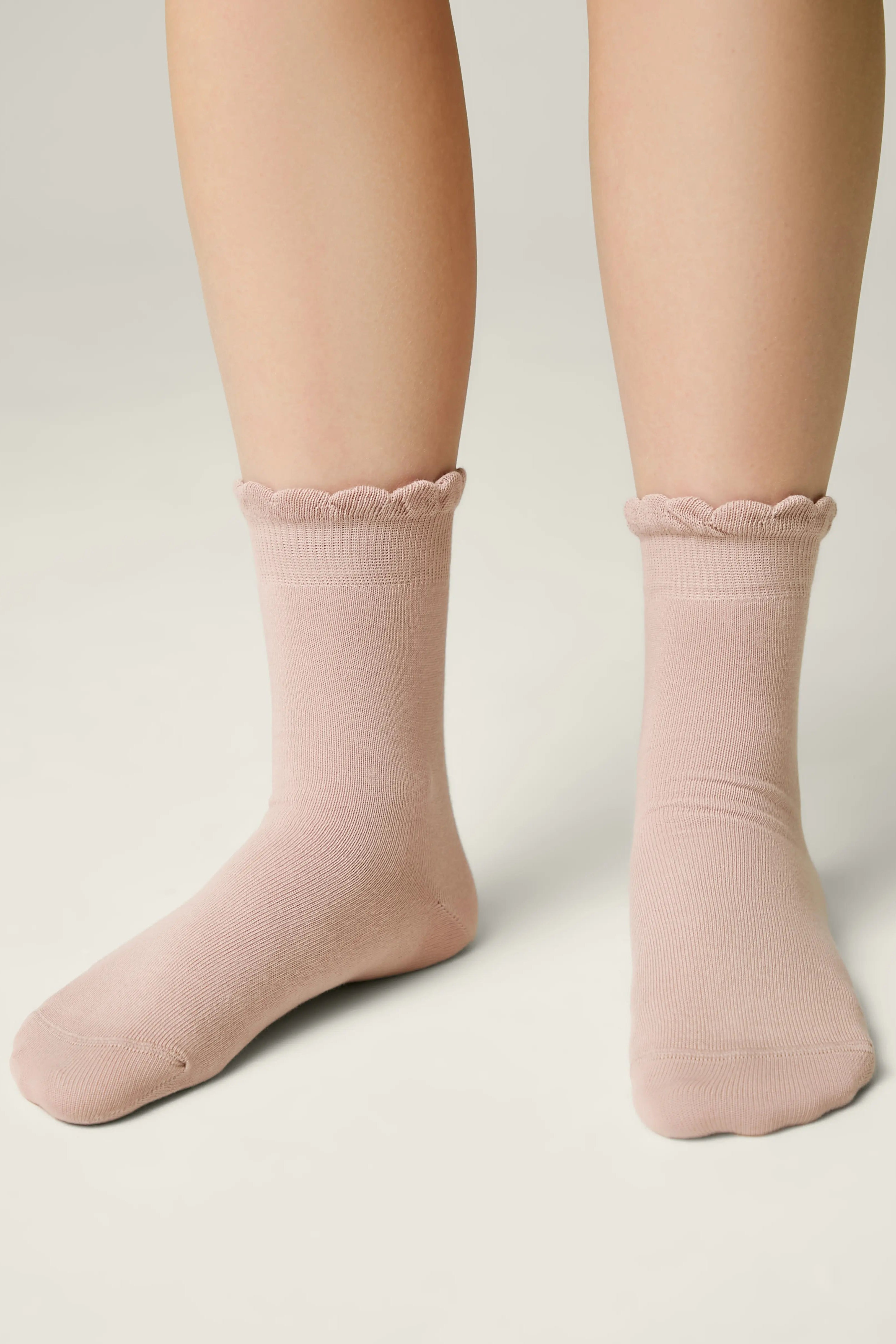 Pink socks with lace trim worn by a person on a neutral background #color_ash-pink