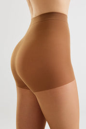 A close-up side view of a model wearing high-waisted ribbed compression shorts in a warm tan shade against a light gray studio background.