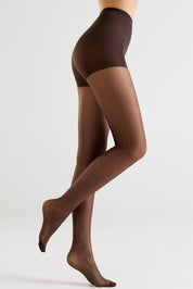 A model's legs wearing sheer dark brown hosiery, shown from the waist down in a side profile against a light gray studio background.