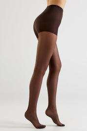 A model's legs wearing sheer dark brown tights, shown from a side-rear angle against a clean light gray studio background.