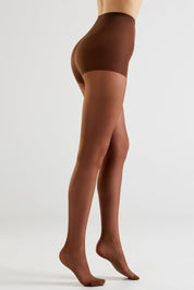 Side view of a model wearing sheer brown tights against a light gray studio background.