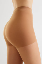 Close-up side view of a model wearing high-waisted ribbed shapewear tights in a warm nude tan color against a light gray studio background.