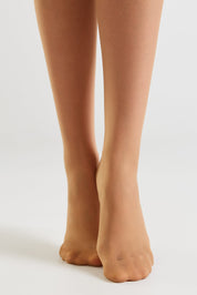 Close-up of a person's legs and bare feet wearing sheer, skin-toned ankle socks against a clean white studio background.