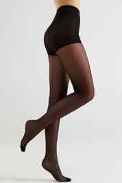 A model's legs wearing sheer black tights, shown from the waist down in a side profile against a light gray studio background.