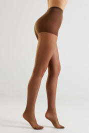 A model shown from the waist down wearing sheer brown hosiery, photographed against a clean light gray studio background.