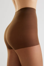 Close-up side view of a model wearing high-waisted brown shapewear briefs against a light gray studio background.