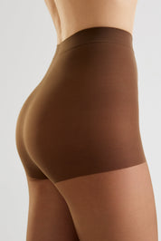 Close-up side view of a model wearing high-waisted brown shapewear briefs against a light gray studio background.