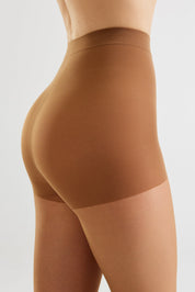 A close-up side view of a model wearing high-waisted ribbed compression shorts in a warm tan shade against a light gray studio background.