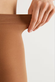 Close-up of a person wearing a ribbed brown hosiery stocking, pulling the waistband slightly outward with a hand against a clean white background.