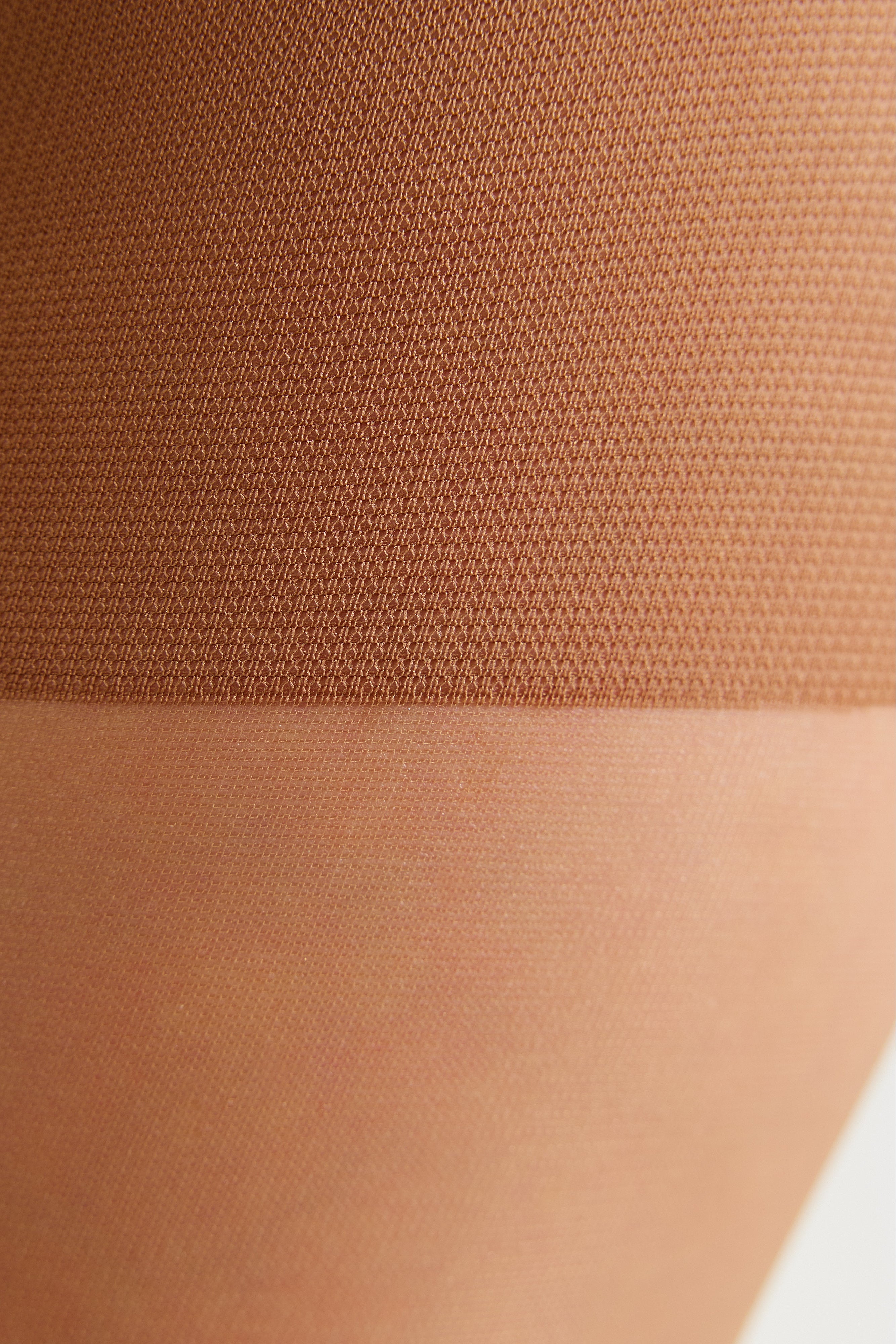Close-up of a sheer hosiery leg band or pantyhose transition area on skin, showing a warm nude/tan color and fine knit texture.