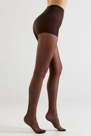 A model's legs wearing sheer dark brown tights, shown from a side-rear angle against a clean light gray studio background.