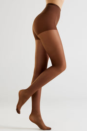 A model's legs wearing sheer brown tights, shown from the waist down in a side profile against a light gray studio background.