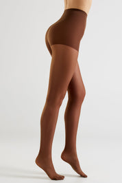 A model's legs wearing sheer brown hosiery, shown from the waist down in a side profile against a light gray studio background.