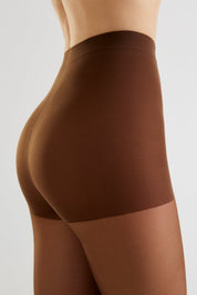Close-up side view of a model wearing a high-waisted brown shapewear brief or compression shorts against a light gray studio background.