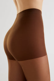 Close-up side view of a model wearing a high-waisted brown shapewear brief or compression shorts against a light gray studio background.