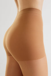 Close-up side view of a model wearing high-waisted ribbed shapewear briefs in a warm nude tan color against a light gray studio background.