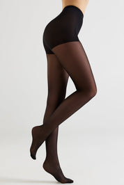 A model's legs wearing sheer black tights, shown from the waist down in a side profile against a light gray studio background.