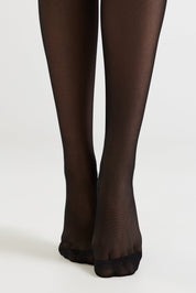 Black sheer hosiery worn on legs, shown from the calves down against a plain light gray studio background.
