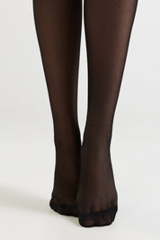Black sheer hosiery worn on legs, shown from the calves down against a plain light gray studio background.