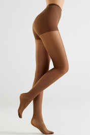 A model's legs wearing sheer brown hosiery, shown from the waist down in a side profile against a light gray studio background.
