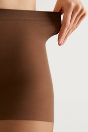 Close-up of a person wearing a brown ribbed compression or shapewear garment, with a hand stretching the elastic waistband against a plain light background.
