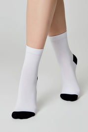 White socks with black toes and cuffs worn by a person on a light gray background