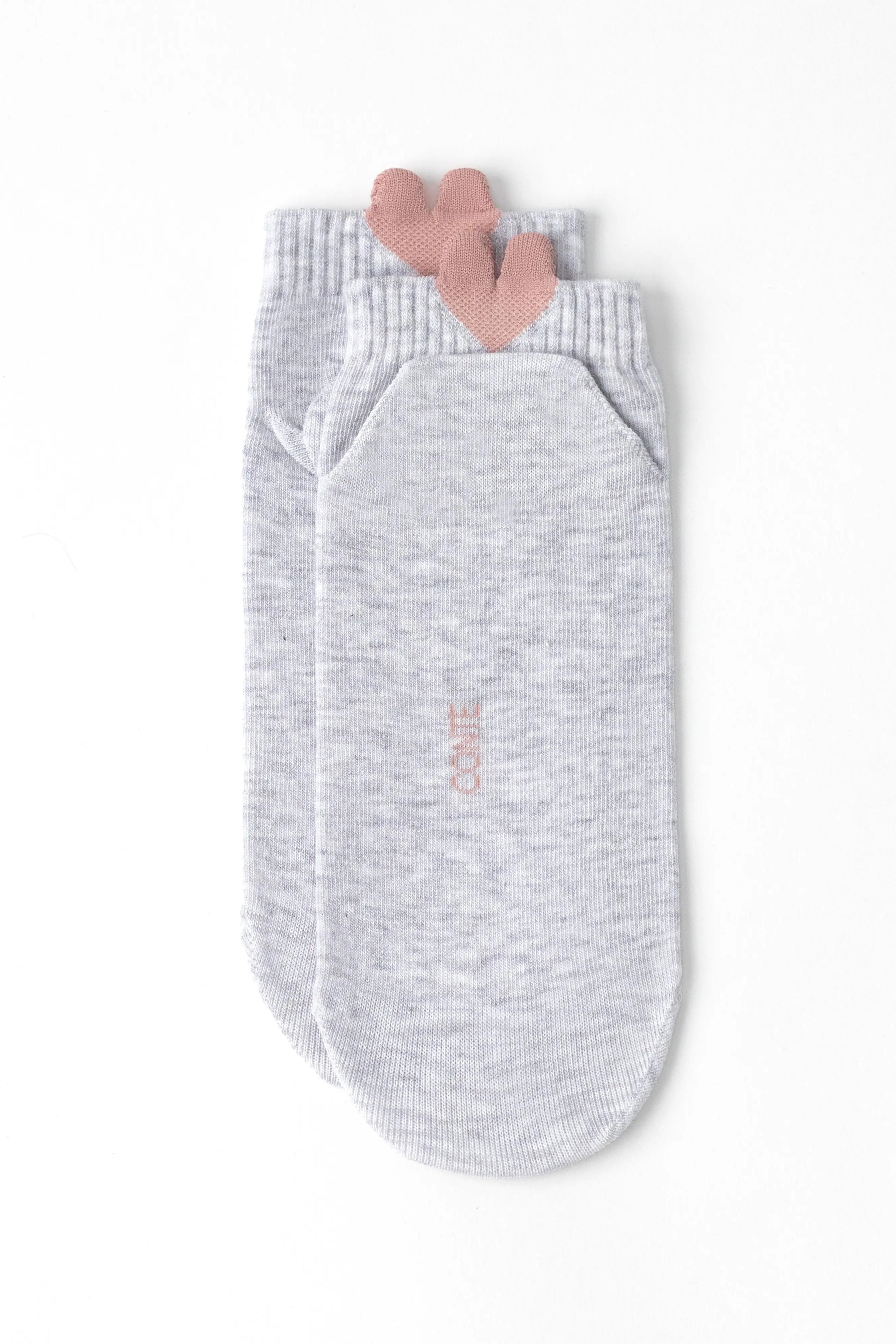 A pair of light heather gray ankle socks with a small pink heart detail at the top cuff and vertical pink 'COOIE' branding on the sole, shown on a clean white background.
