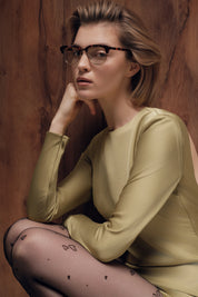 Woman wearing glasses and a green dress with a wooden background