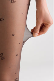 Sheer stockings with heart patterns being pulled up by a hand on a light background
