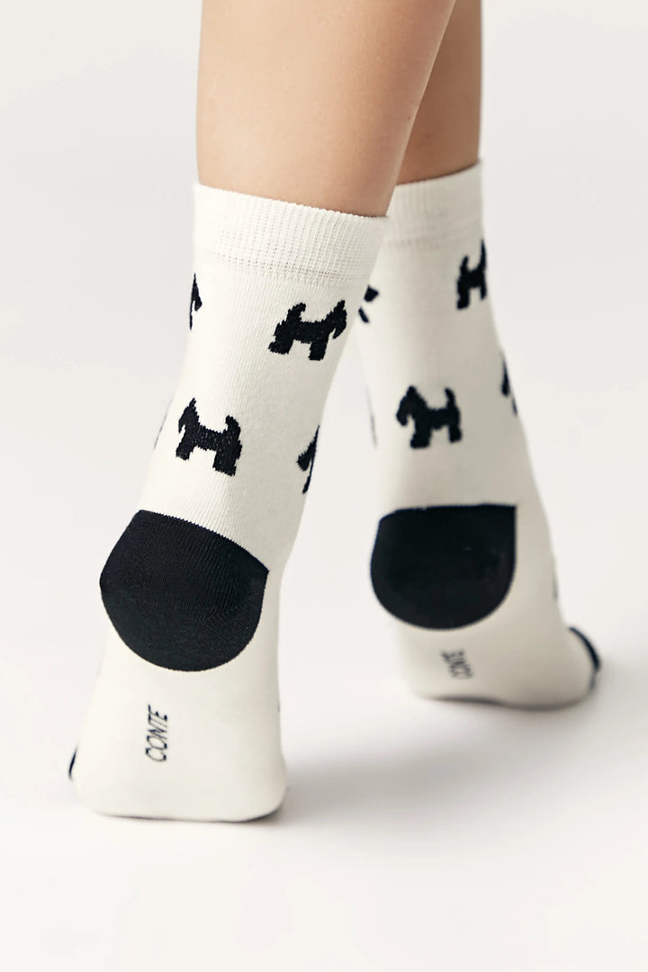 White socks with black dog pattern worn by a person on a white background #color_milk