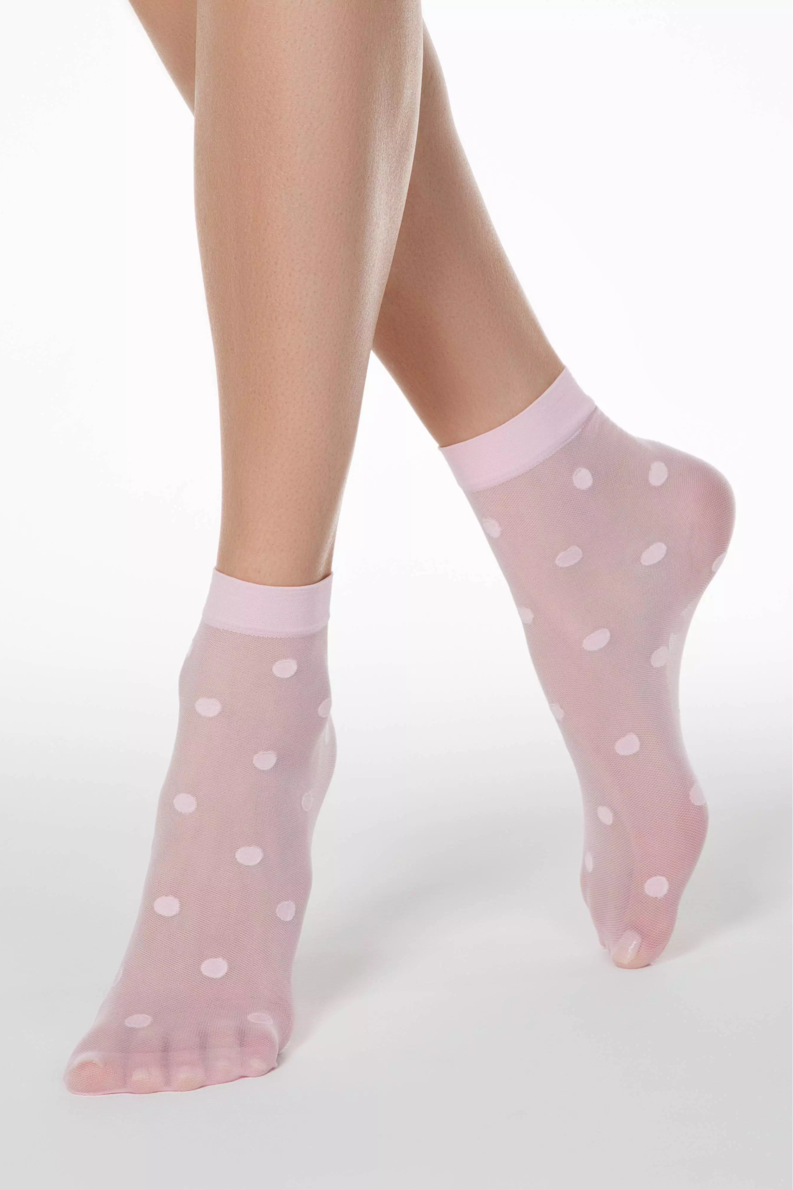 Pink sheer socks with white polka dots worn by a person on a light gray background #color_light-pink