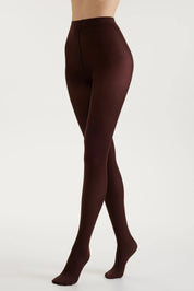 A model's legs wearing dark brown tights, shown from the waist down in a side profile against a clean white studio background.