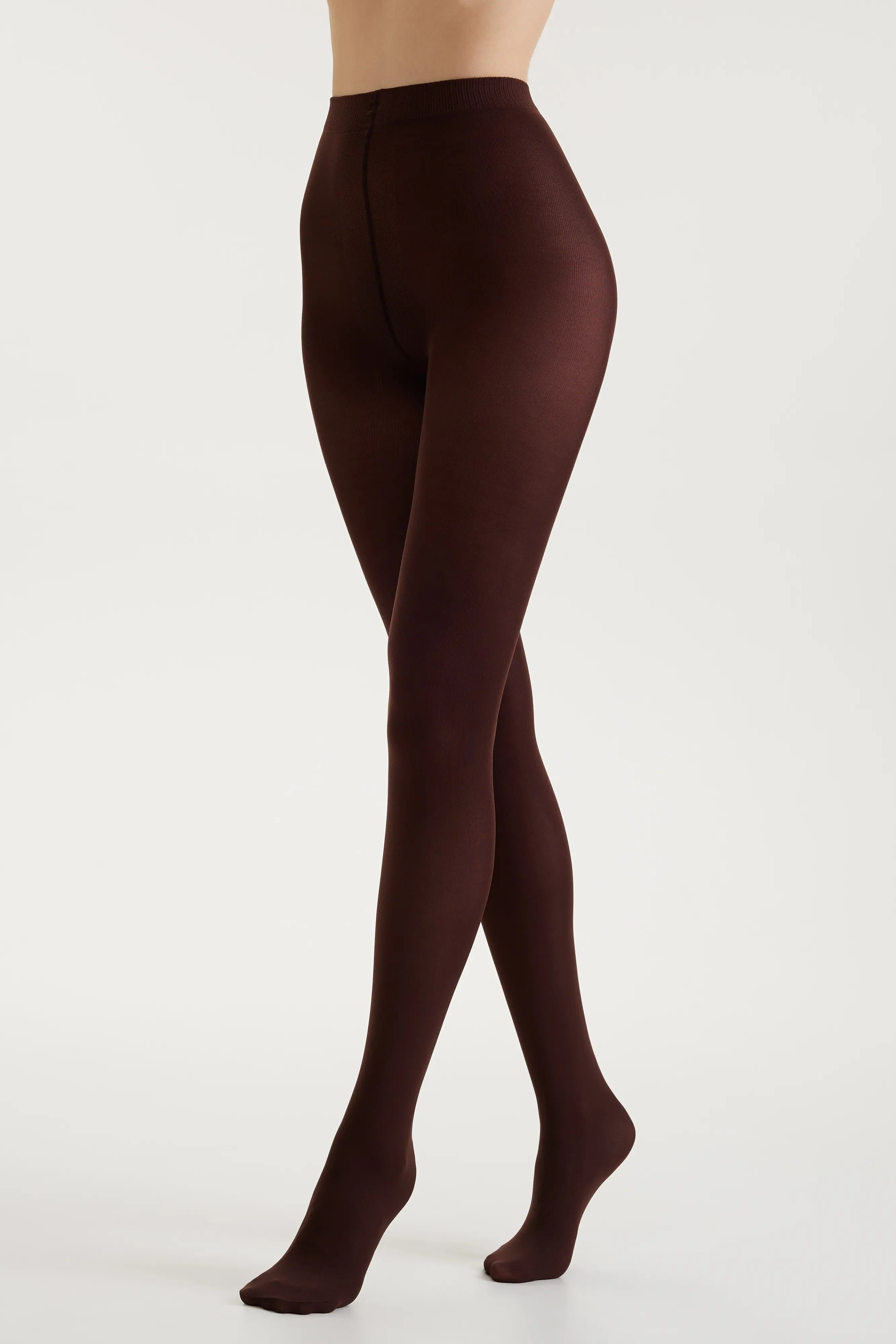 A model's legs wearing dark brown tights, shown from the waist down in a side profile against a clean white studio background.