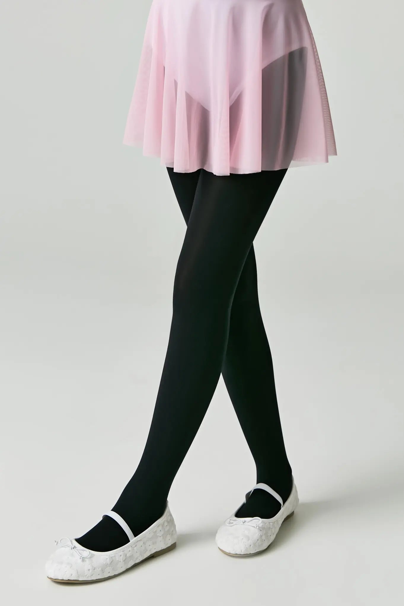 Person wearing black tights and white shoes on a plain background #color_nero-black