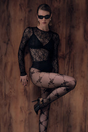 Woman wearing a black lace bodysuit and stockings against a wooden background