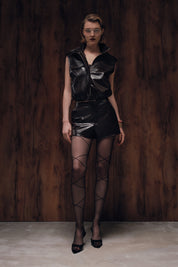 Model wearing a black leather outfit with fishnet stockings against a dark wooden background