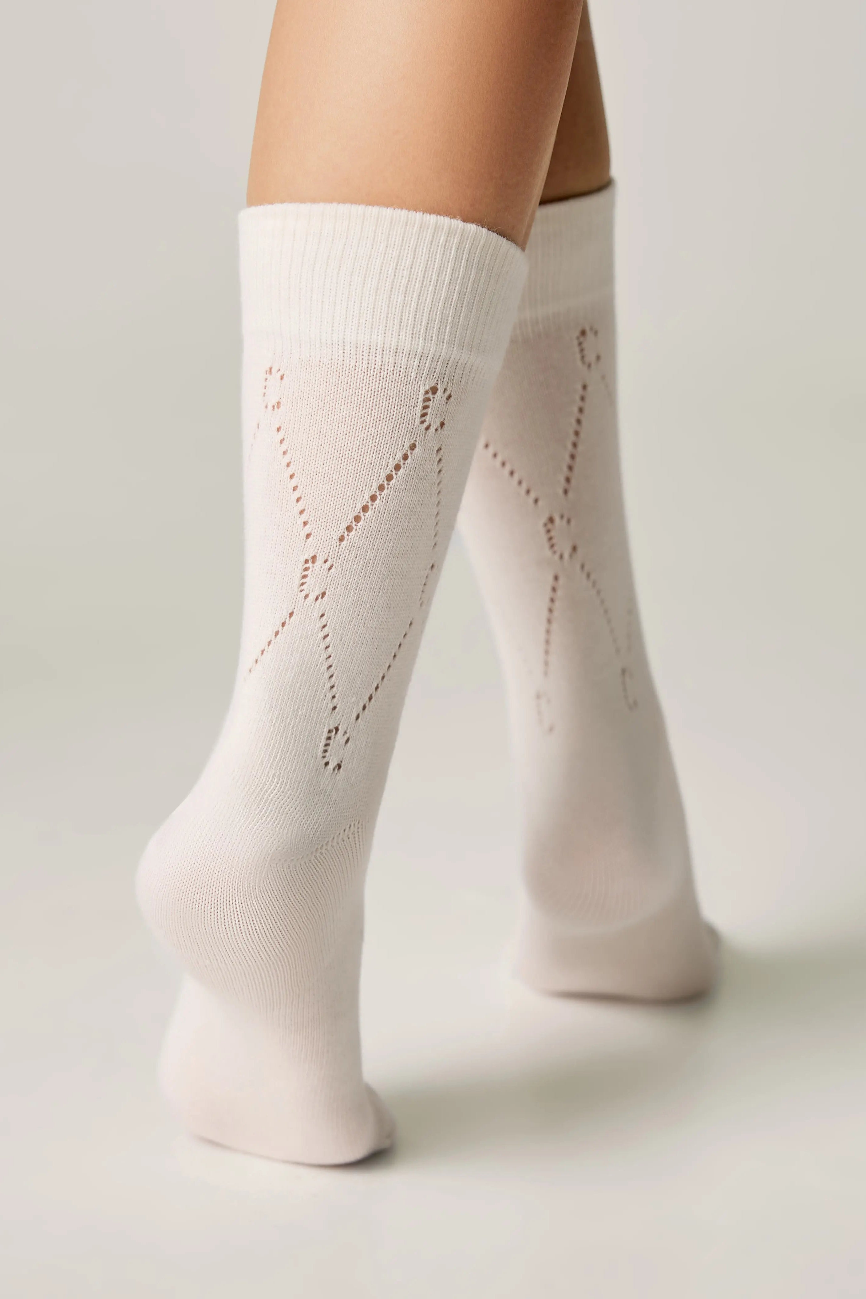 White knee-high socks with subtle pattern worn by a person on a light background #color_milk